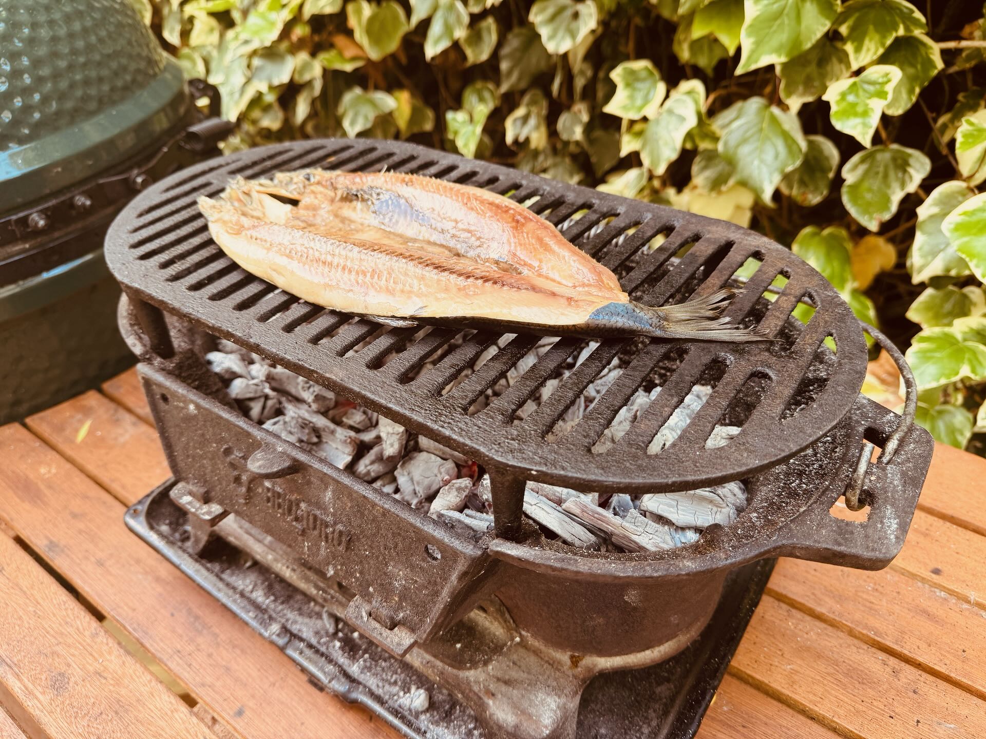 Smoked fish on a cast-iron grill over glowing lumpwood charcoal